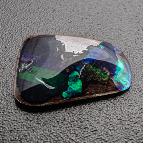 Boulder Opal aus Australien. 0,98 Karat. Dünnes Plättchen mit sehr schönem Farbenspiel. Vorsichtig handhaben, fassen und tragen.